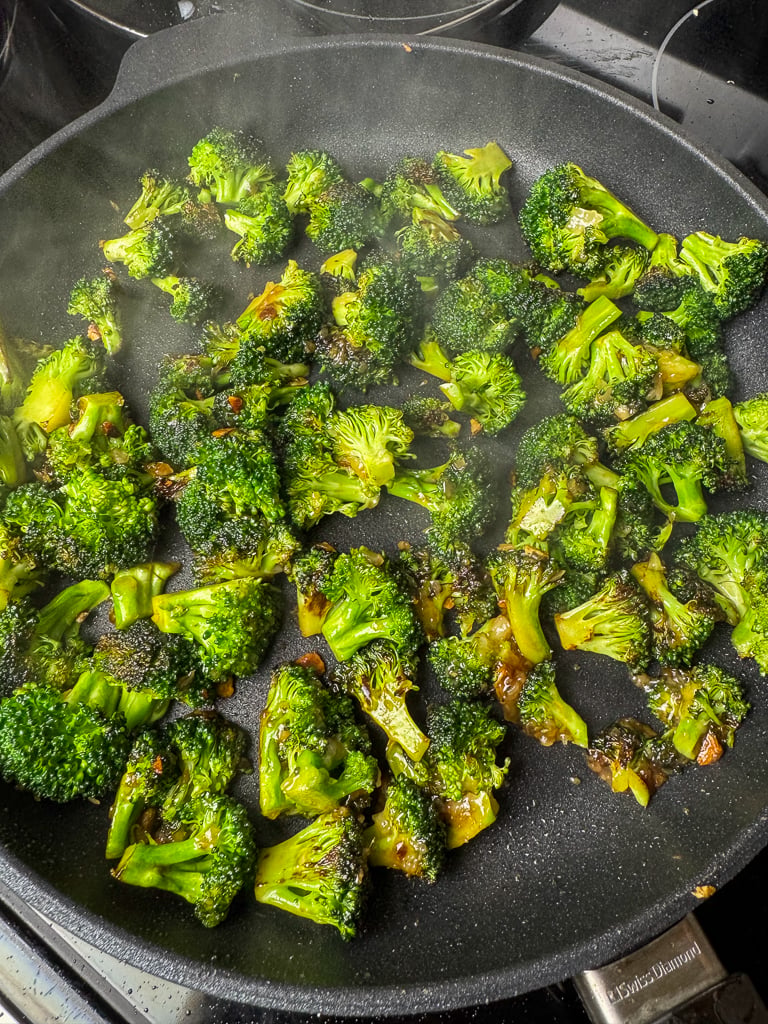 Broccoli browning in a oil, garlic and ginger with soy sauce in a black skillet.