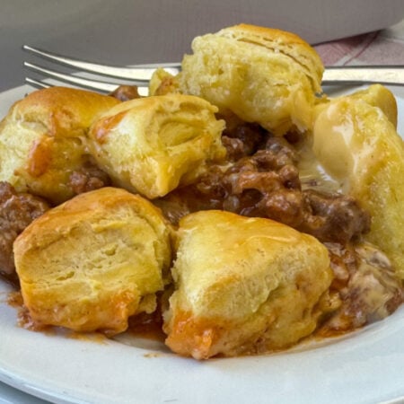 Close up of a plate full of flavorful mixture of hamburger, onion and tomato sauce with cheese melted in between a layer of flaky biscuit pieces.