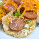 Close up cheesy Pierogi enhanced with Kielbasa, onions and sour cream while baking in beef broth with a fork underneath.