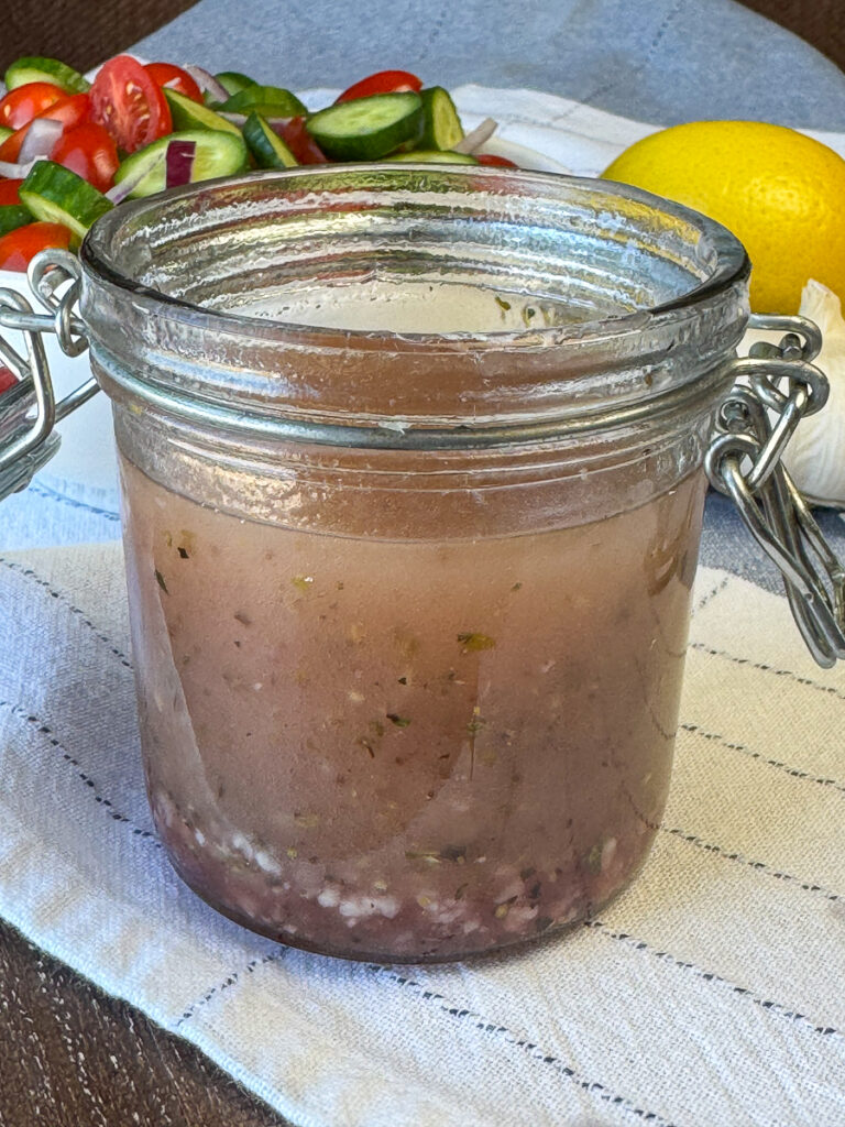 Glass jar with homemade dressing for Greek pasta salad on a blue and white napkin.