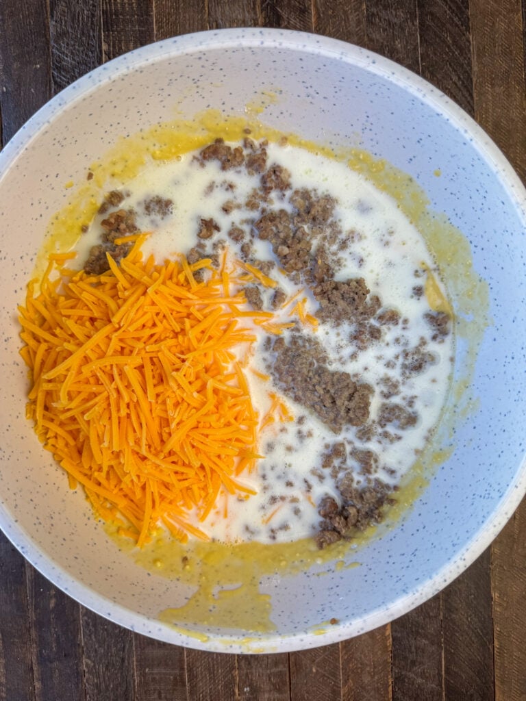 Mixing bowl with scrambled eggs, milk, sausage and shredded cheddar cheese.