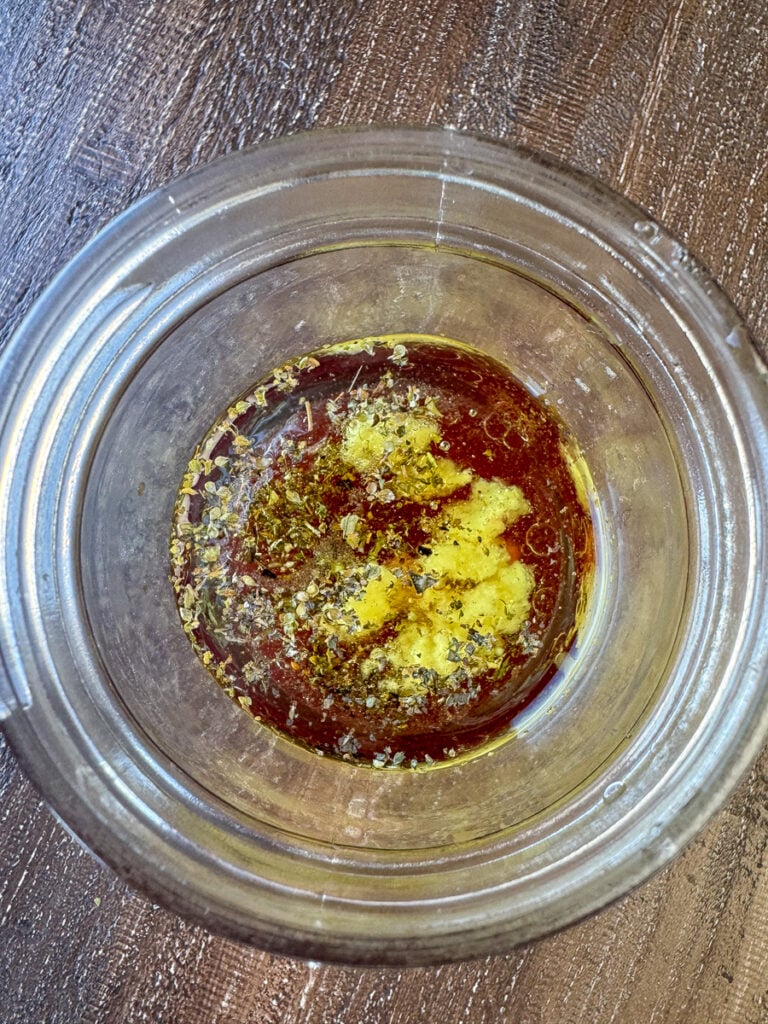 Overhead view of a jar with ingredients for homemade Greek salad dressing ready to shake and serve.
