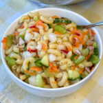 Crunchy and delicious chopped vegetables mixed into macaroni coated in Italian dressing in a small white bowl.