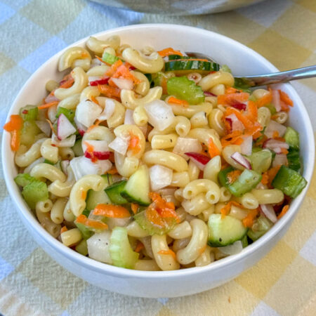 Crunchy and delicious chopped vegetables mixed into macaroni coated in Italian dressing in a small white bowl.