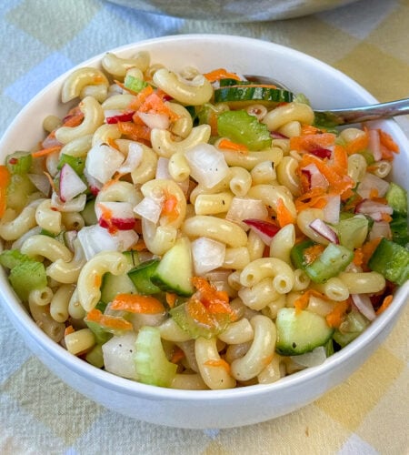 Crunchy and delicious chopped vegetables mixed into macaroni coated in Italian dressing in a small white bowl.