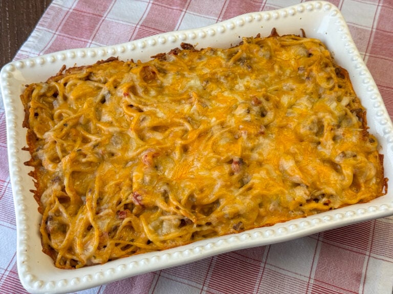 Side view of cheese melted over taco seasoned spaghetti with ground beef and veggies to make an easy meal on a red and white plaid napkin.
