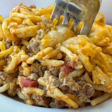 Close up pieces of spaghetti coated with cheese and filled with tender bites of ground beef and chopped tomatoes.