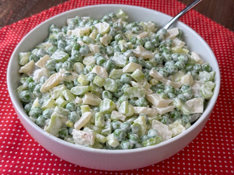 Creamy dressing topping peas with crunchy water chestnuts and celery mixed into a bowl full of the cold salad on a red napkin.