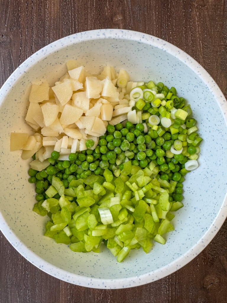 Frozen peas, chopped celery, water chestnuts, and sliced green onion in a mixing bowl.