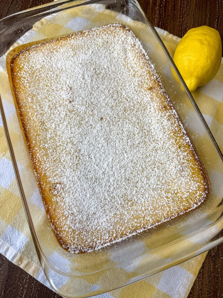 Overhead view of a pan of easy homemade lemon bars in a 9 x 13" glass pan on a yellow and white plaid napkin with a lemon beside the pan.