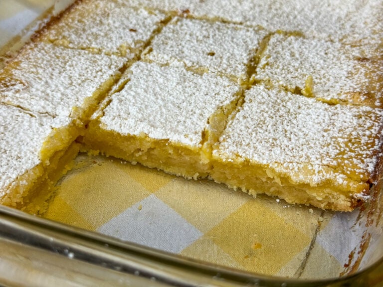 Side view of a glass pan of lemon squares dusted with powdered sugar.