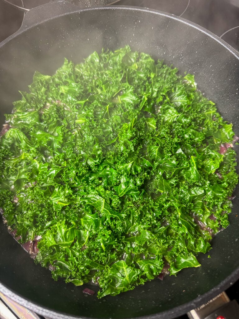 Chopped kale cooking in a frying pan with onions and broth for 3 minutes.