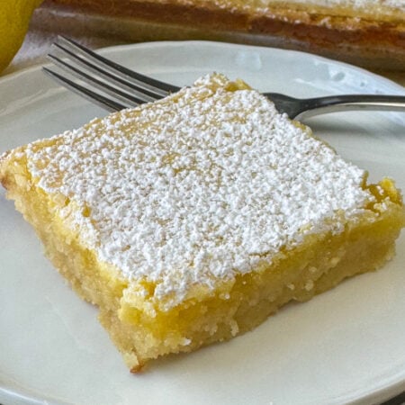 Close up of powdered sugar dusted on a gooey lemon filling on a buttery crust in a delicious lemon square.