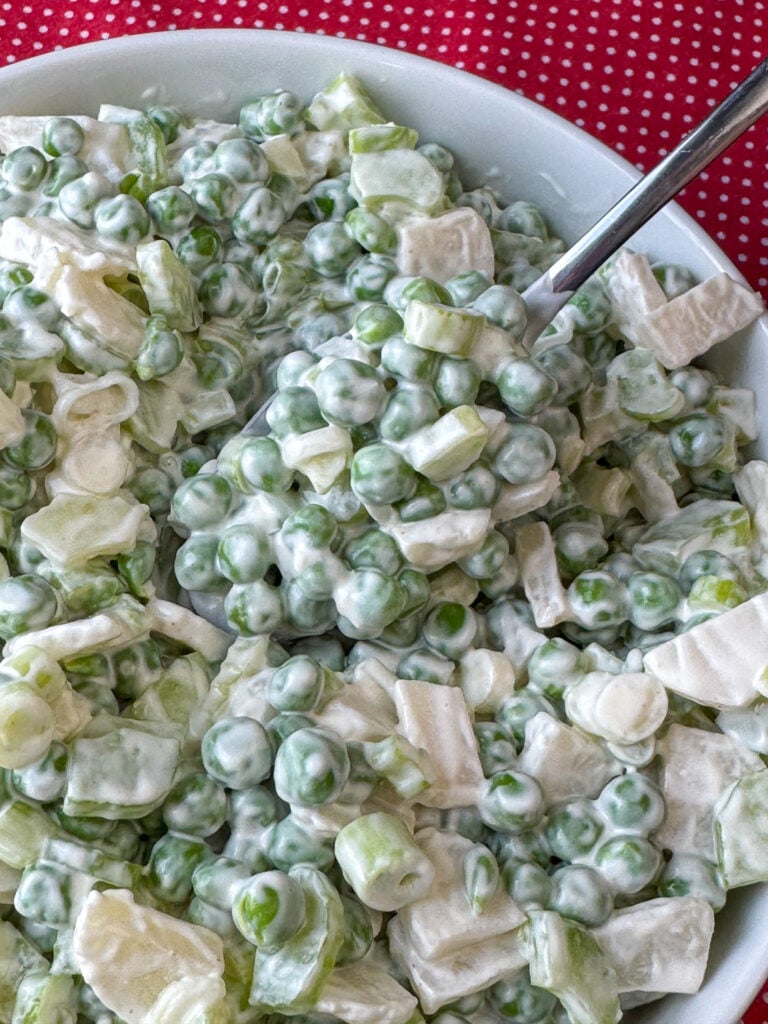 Close up spoon full of old fashioned pea salad with a light dressing and a couple other veggies mixed in.