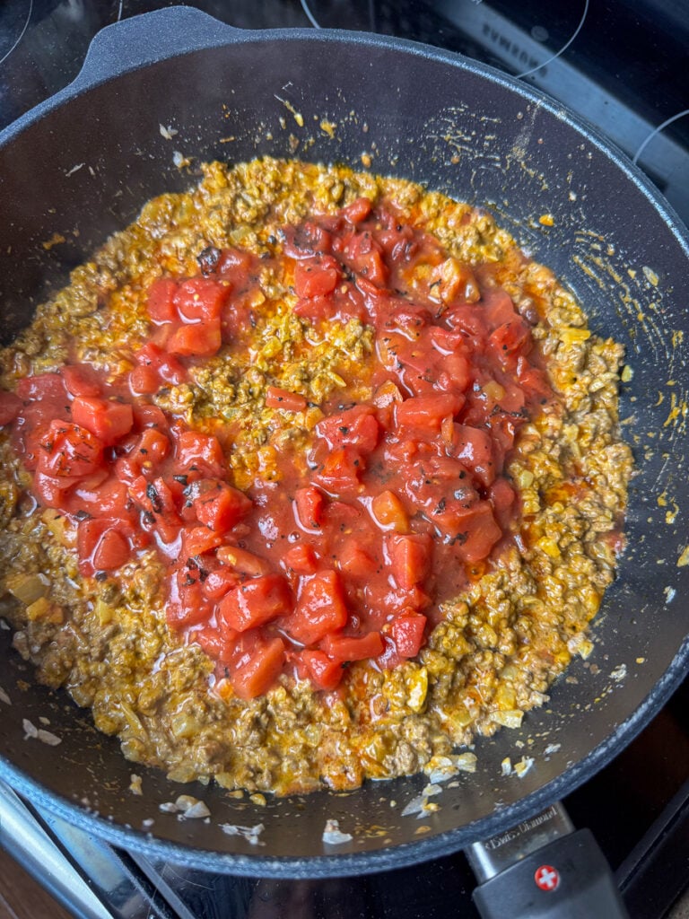 Fire roasted tomatoes added to a skillet to make taco spaghetti.