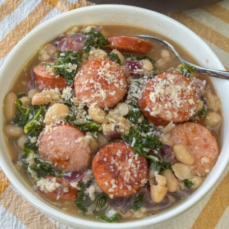 Simple seasonings with canned white beans, Kielbasa sausage, kale, onions and garlic in a bowl with a spoon ready to eat.