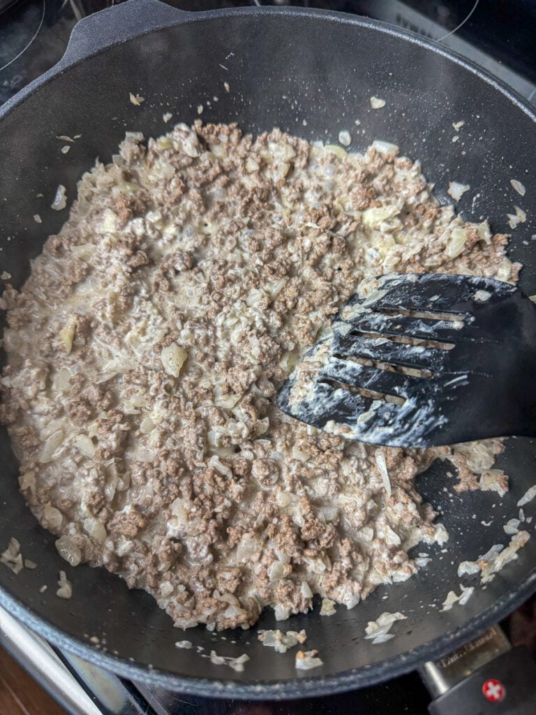 Cream cheese melting into a skillet with hamburger and onions.
