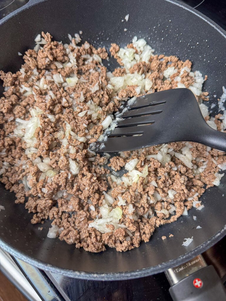 Spatula stirring chopped onion into browned ground beef.