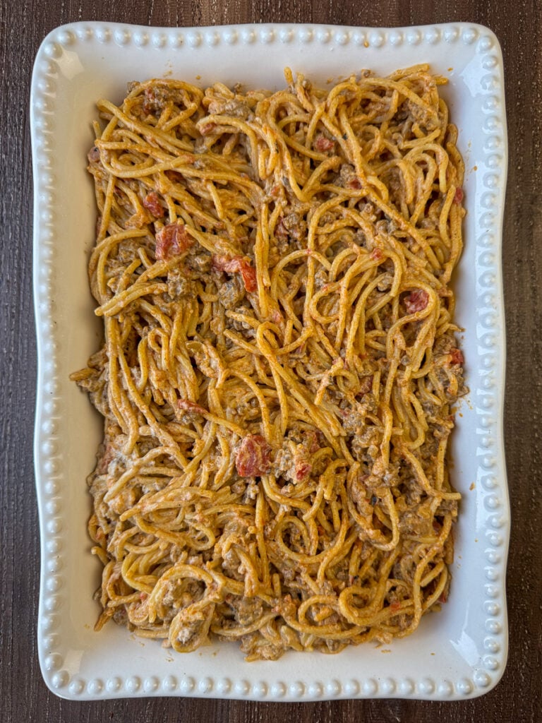 Rich cream cheese coated spaghetti with beef and tomatoes nestled in for plenty of creamy flavor spread in a casserole dish.