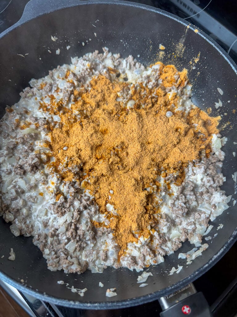 Taco seasoning added to a skillet of ground beef, onions and cream cheese.