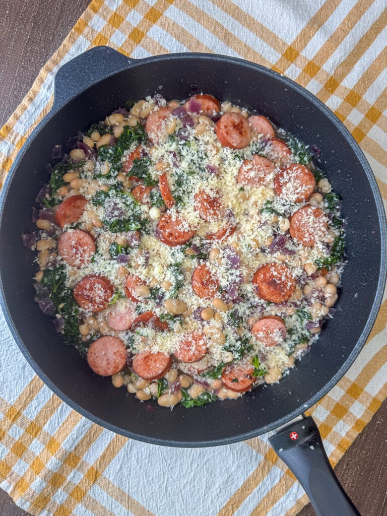 Overhead view of Parmesan cheese sprinkled on an easy smoked sausage and beans skillet meal on a yellow and white napkin.
