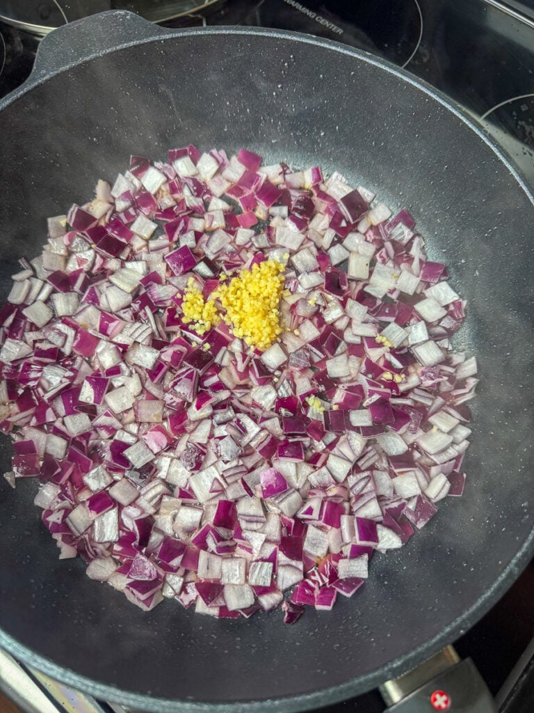 Minced garlic added to chopped red onion in a skillet.