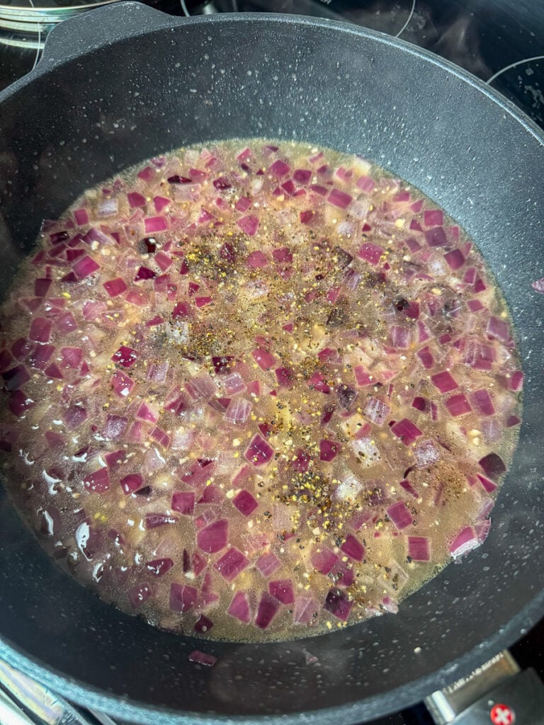 Onion simmering in broth and seasoned with salt and pepper.