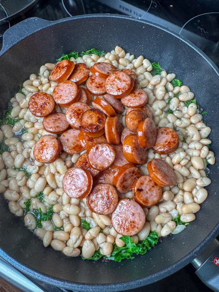 Browned slices of sausage added to white beans and kale in an easy skillet meal.