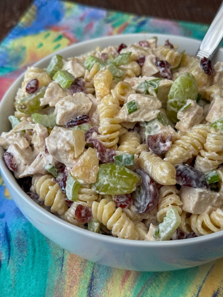 Overhead view of cashews, chicken and grapes nestled in twist pasta with an easy dressing made of ranch and mayo in a bowl on a pastel napkin.