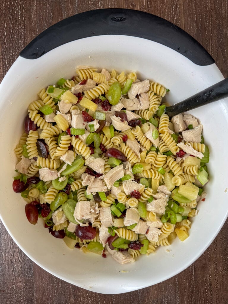Overhead view of chicken and pasta stirred into grapes and other fruit in a white bowl.