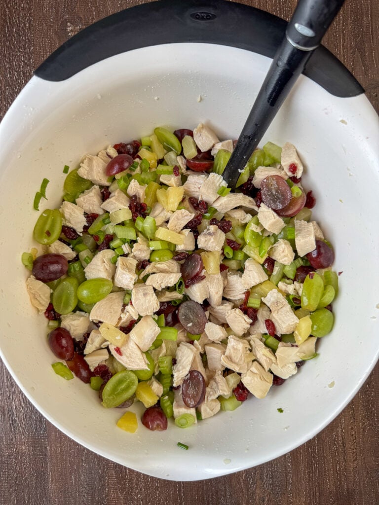 Red and green grape halves stirred into cubed chicken in a large mixing bowl.