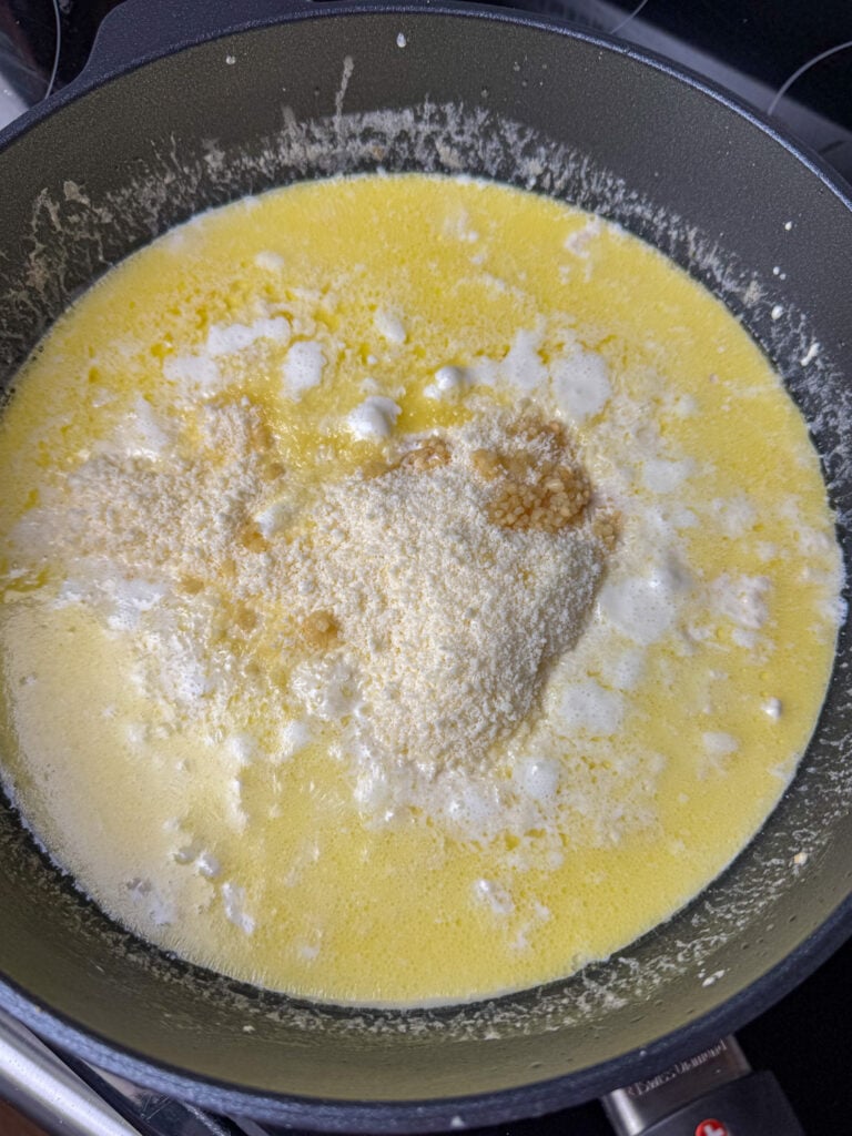 Grated parmesan cheese, minced garlic and heavy cream added to a skillet with cream cheese and butter to make a white pasta sauce.