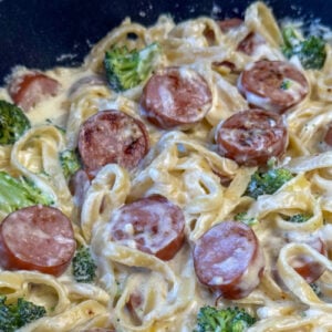 Close up of a pot full of Polish Kielbasa and broccoli stirred into pasta with a simple cream sauce.