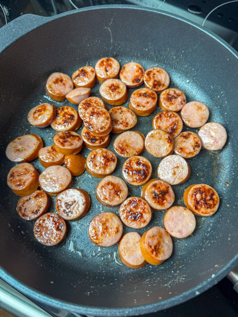 Slices of Kielbasa frying in butter in a skillet.