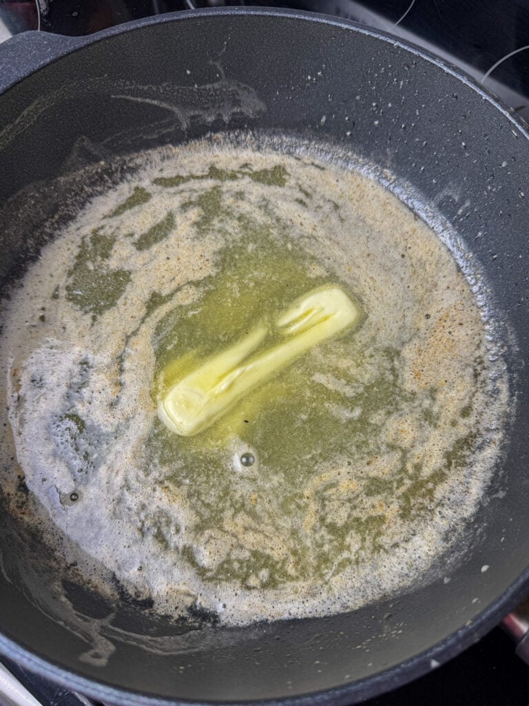 A stick of butter almost melted in a skillet.
