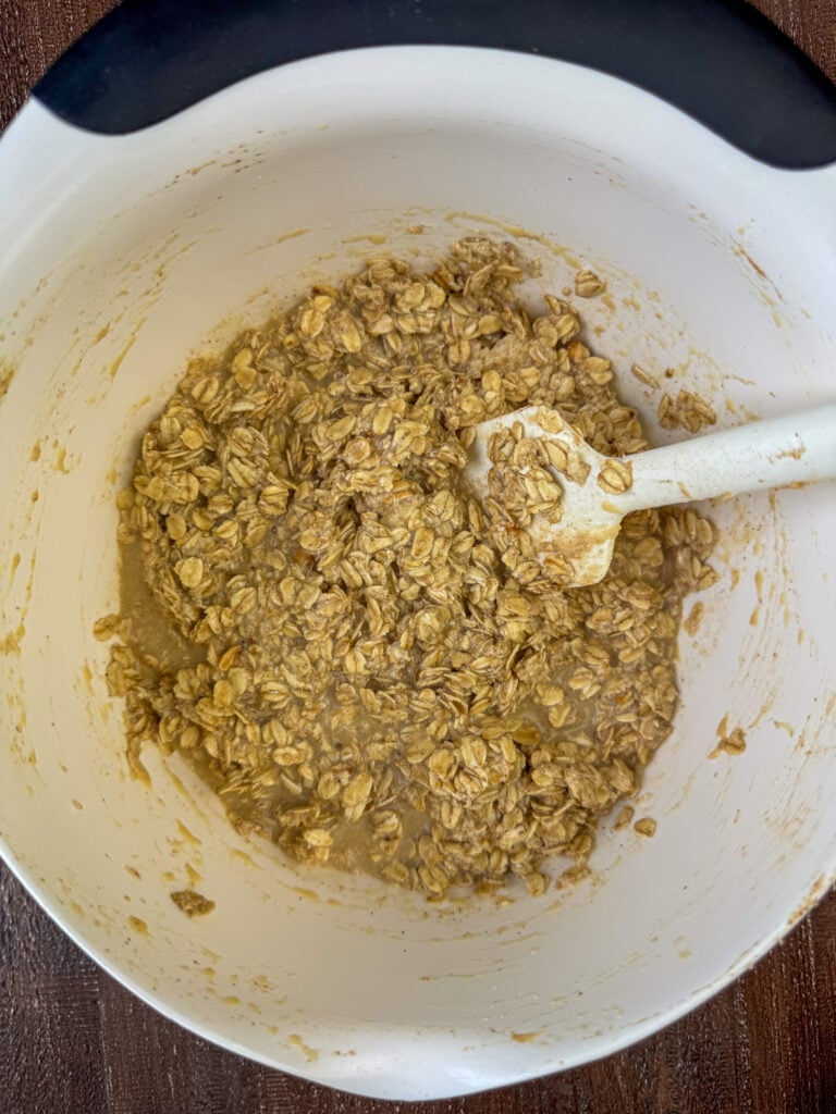 Milk, baking powder, salt, cinnamon and old fashioned oats being stirred together in a bowl with a spatula.