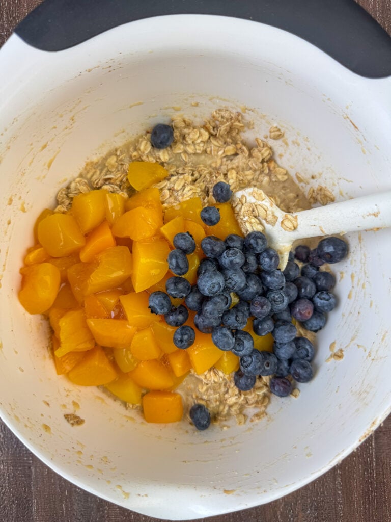Chopped canned peaches and fresh blueberries added to a bowl with oatmeal.