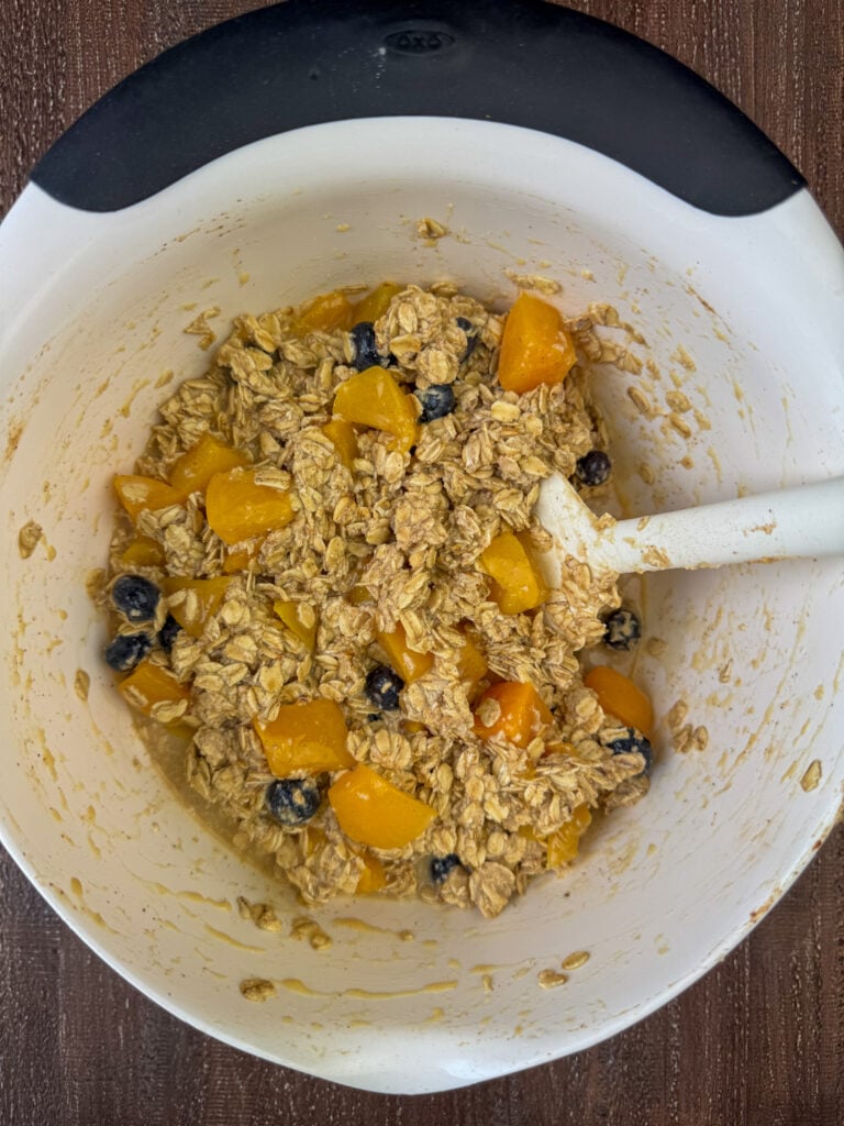 Spatula stirring peaches and blueberries into an oatmeal mixture.