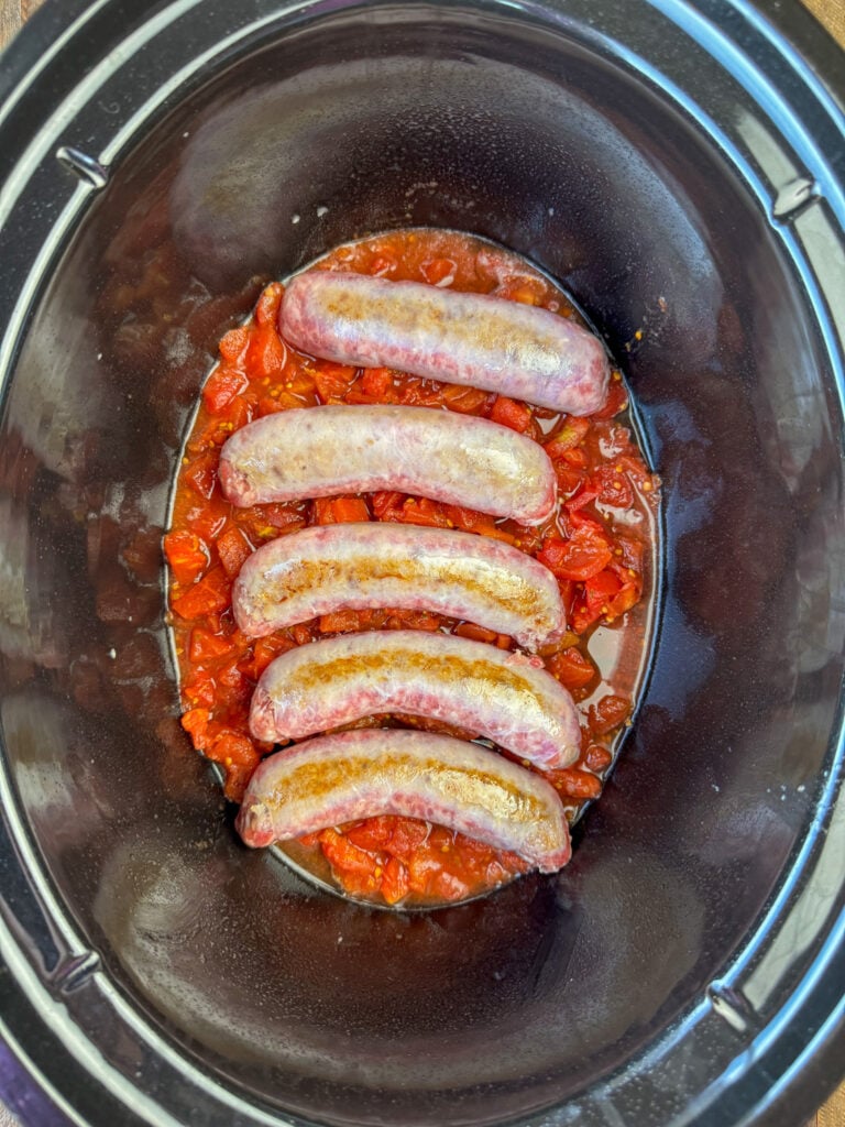 Browned brats on a can of diced tomatoes with juice in the slow cooker.