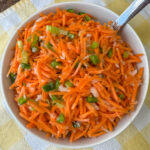 Overhead view of shredded carrot salad in a bowl with celery nestled in.