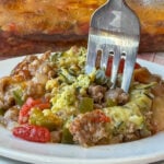 Close up of a fork in a flavorful and easy baked sausage and zucchini casserole with onions, tomatoes and green peppers nestled in and melted cheese on top.