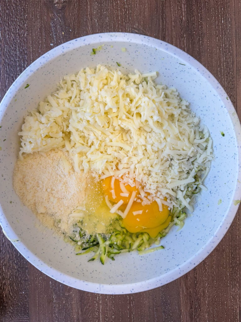 Italian cheese, parmesan cheese and eggs in a mixing bowl over a thick layer of shredded zucchini.