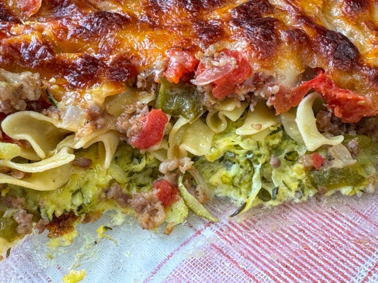 Shredded zucchini baked with a layer of noodles, sausage and cheese on top in a glass casserole dish.
