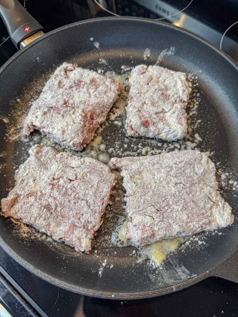 Flour coated Amish crumb steaks browning in a non-stick skillet.