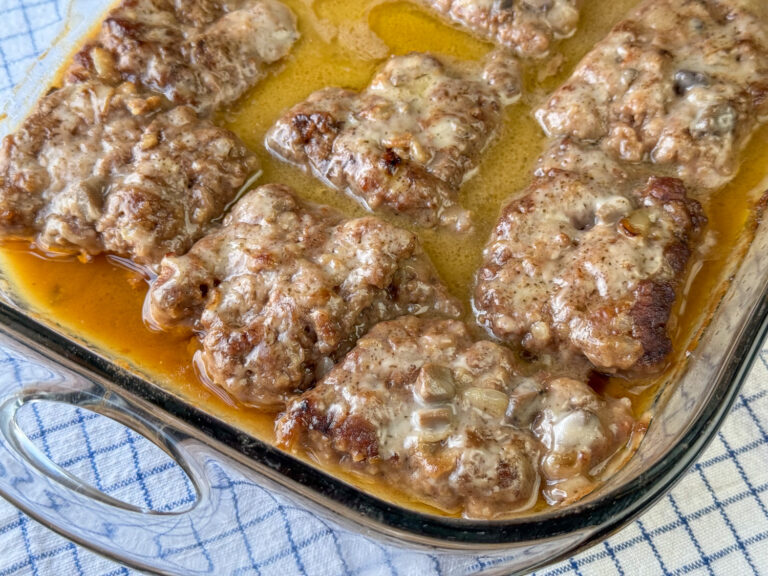 Close up steaks with a generous amount of gravy and chopped mushrooms resting on the flavorful Amish hamburger steak bake.