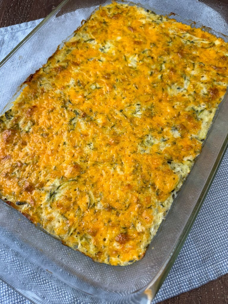 Tender zucchini baked into a savory mixture of cheese, chopped onions and eggs to make a delicious side dish on a blue and white napkin.