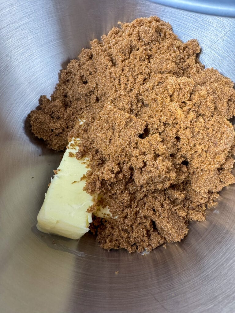 Dark brown sugar poured over a stick of softened butter in a mixing bowl.