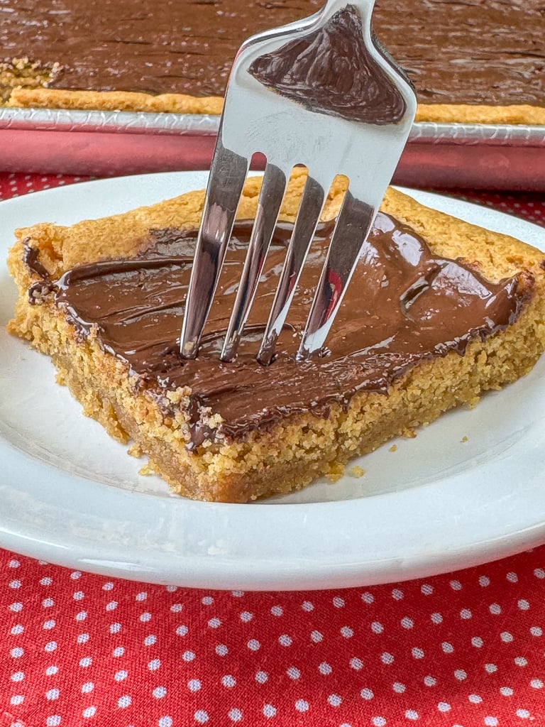 Fork ready to take a bite of an old fashioned peanut butter cookie bar with a silky crumb on a white plate.