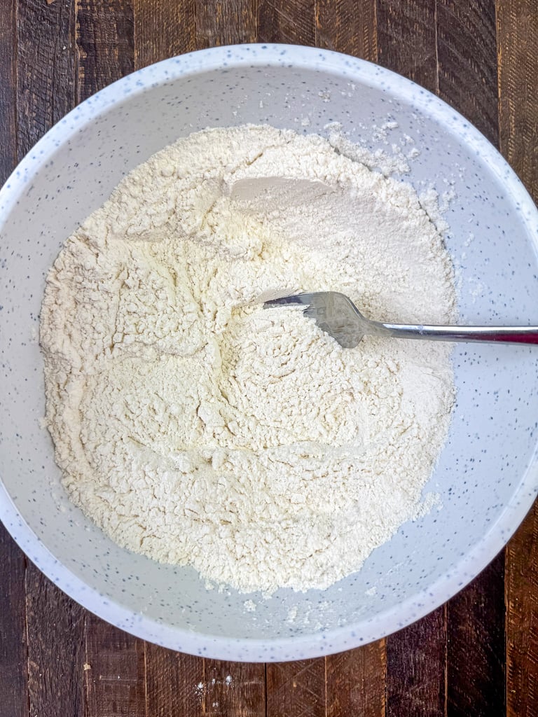 Fork sifting dry ingredients with flour in a mixing bowl.
