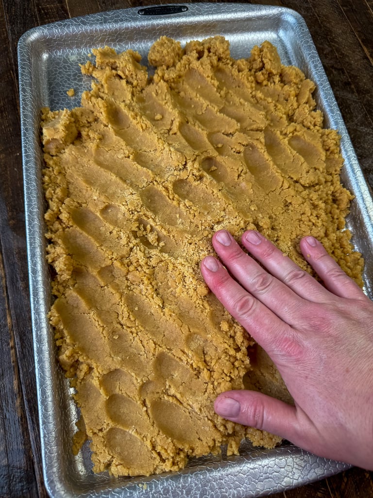 Fingers pressing peanut butter cookie dough in a jelly roll pan.